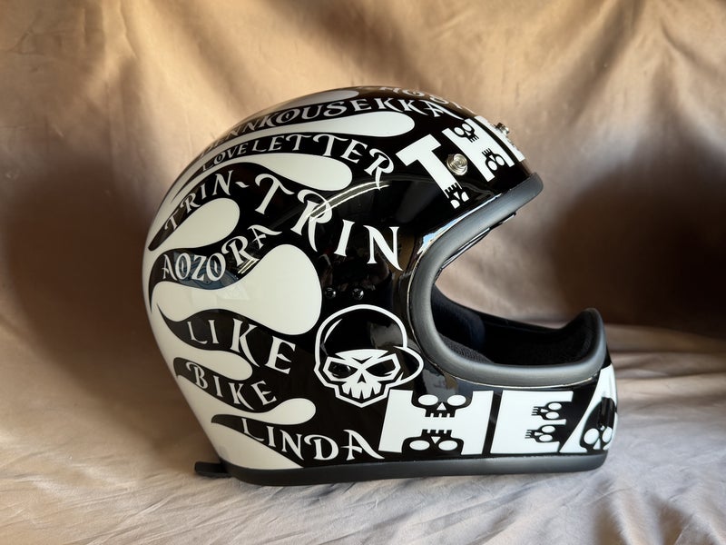 黒いヘルメットの側面に白い英字レタリングと流線形の模様、スカルを配置した実作品写真
