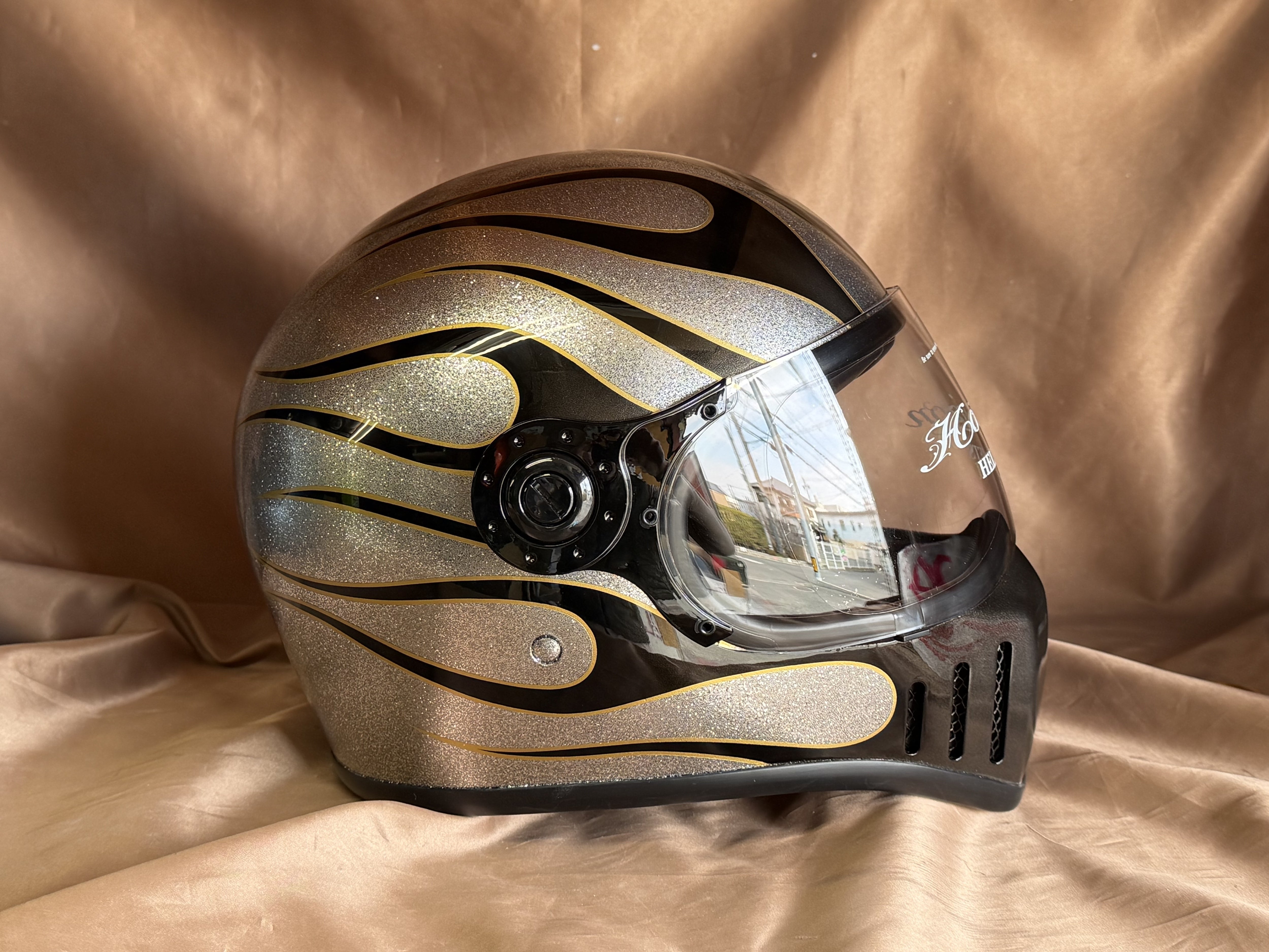 シルバーラメのベースに黒いファイヤーパターンと細い金色の縁取りを描いたフルフェイスヘルメットの施工写真